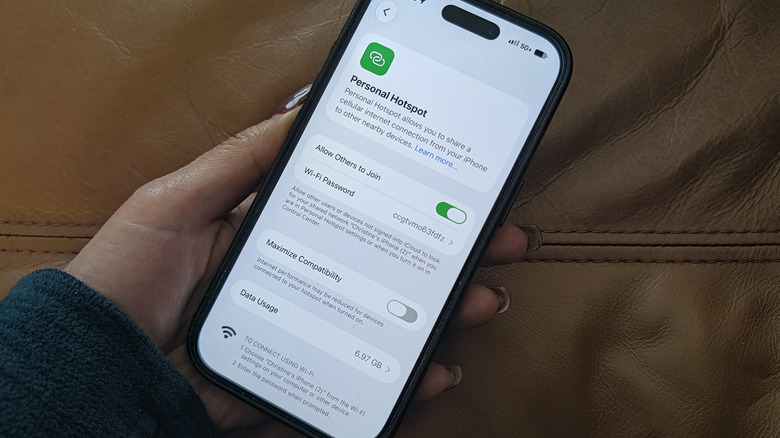 A hand holding an iPhone showing the Personal Hotspot menu.