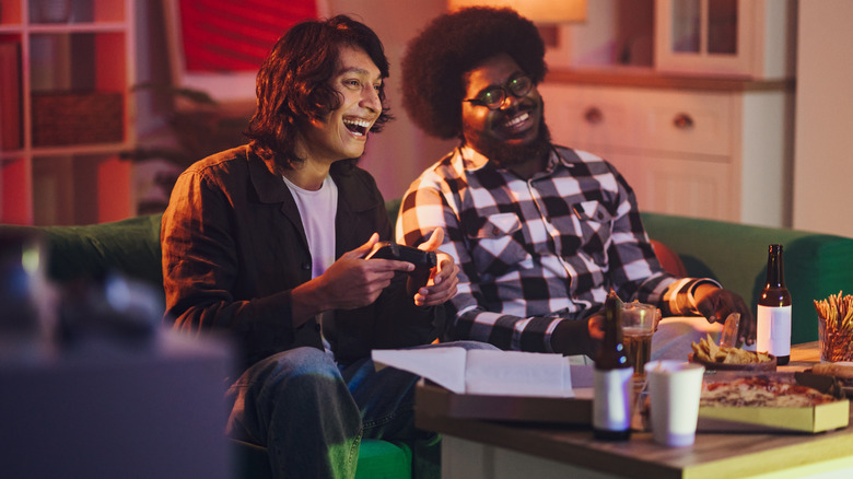 Friends playing a game console with controllers in hand and food on the table.